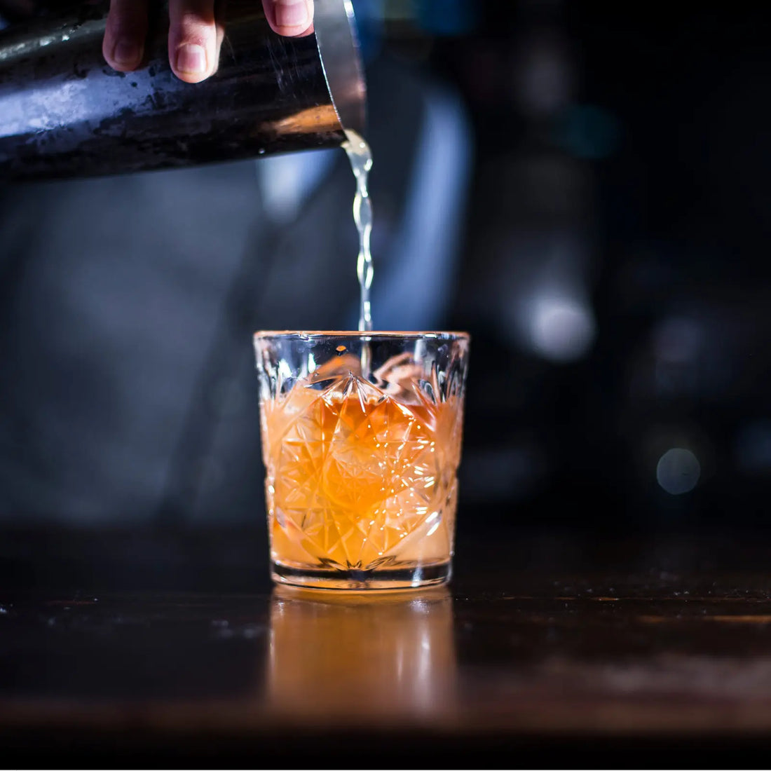 Bourbon Old Fashioned being poured from a shaker into an intricately designed glass with ice