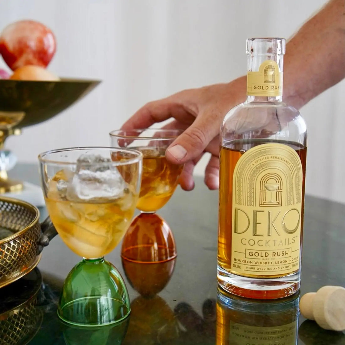 Deko Cocktails Gold Rush bottle and two chilled glasses of bourbon cocktail on a stylish table.