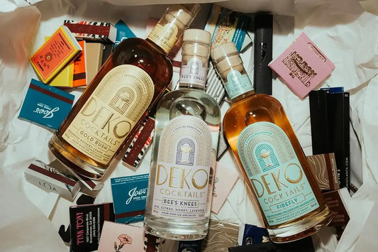 Bottled Gold Rush cocktail from Deko Cocktails, surrounded by matchboxes and packaging on crinkled white paper