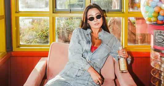 Ready-to-drink cocktail bottle held by a stylish woman in denim and sunglasses, lounging in a retro-themed room.