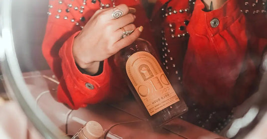 Ready-to-pour cocktail bottle of DEKO Gold Rush held in hand, reflected through a vanity mirror