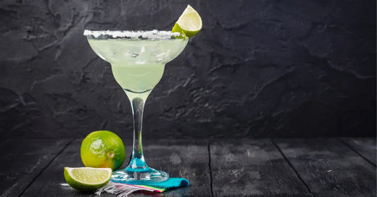 Summer cocktails served in a salt-rimmed glass with fresh lime garnish and whole limes on the table.