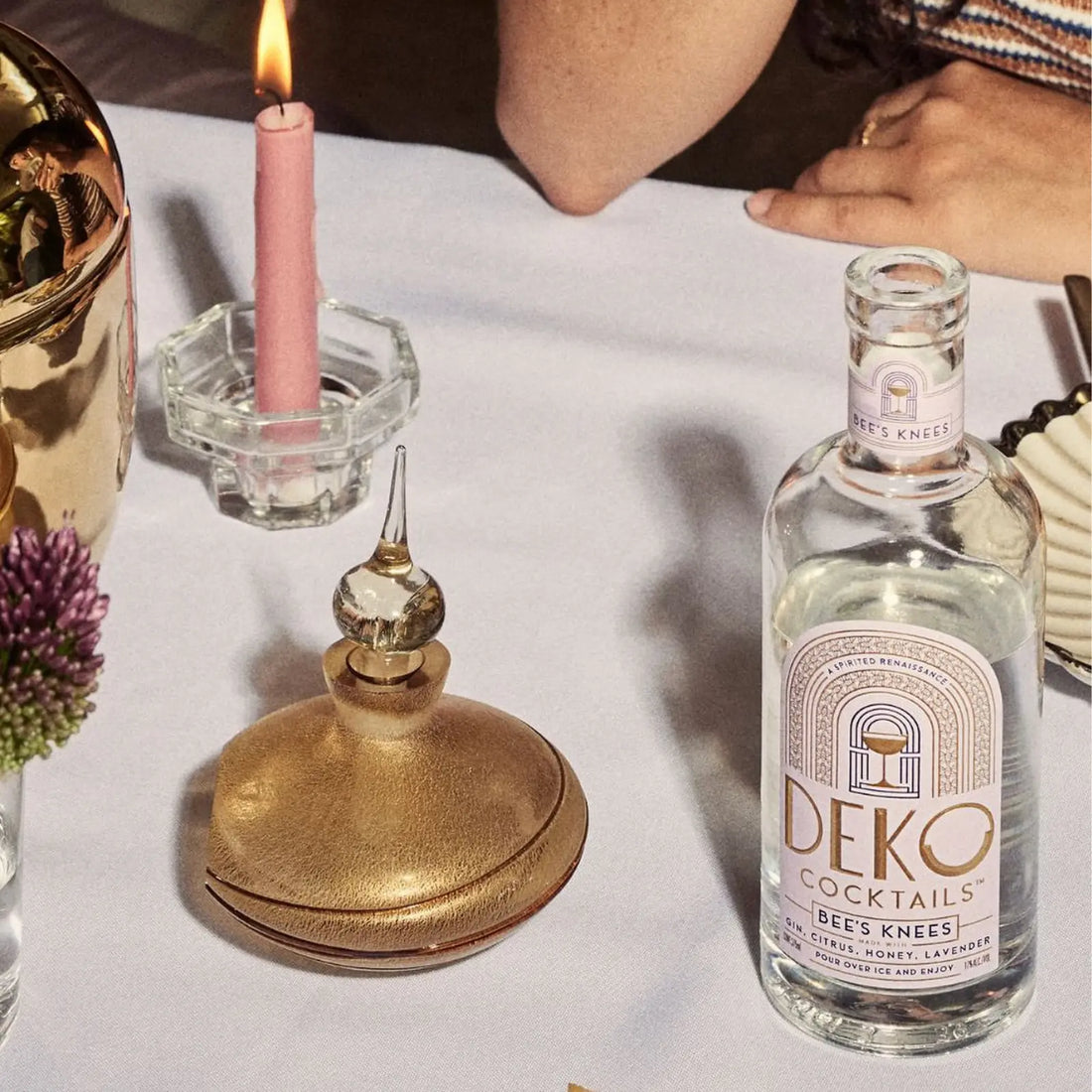Deko Cocktails Bee's Knees bottle placed elegantly on a candlelit dinner table with gold accents.