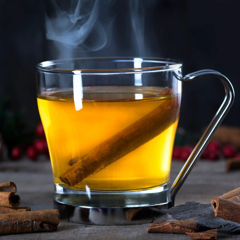 Steaming bourbon hot toddy in a glass mug with a cinnamon stick and cranberries.