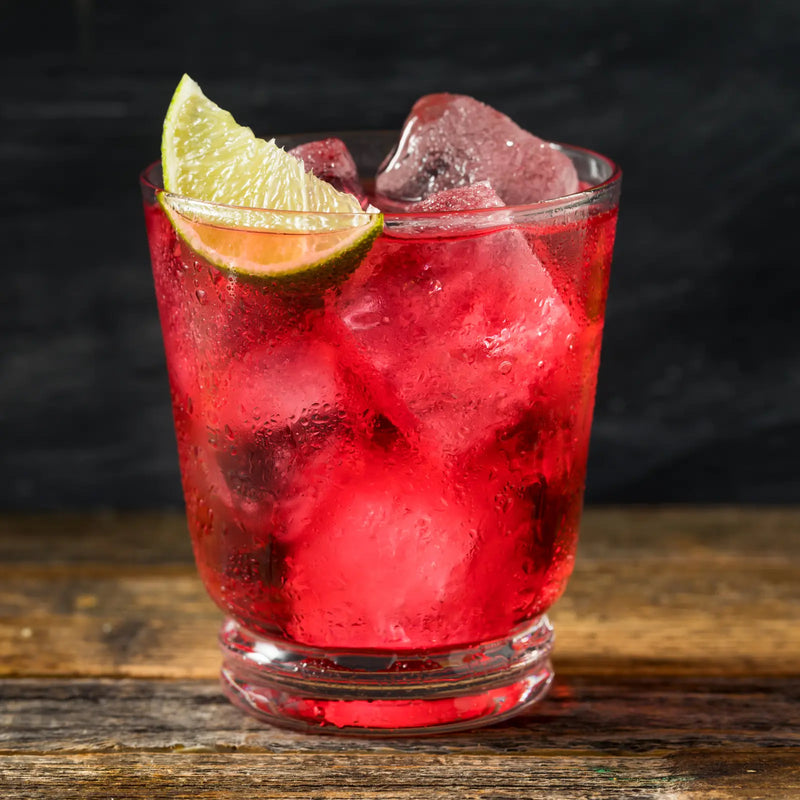 Crimson cranberry vodka cocktail over ice, garnished with a lime wedge on rustic wood.