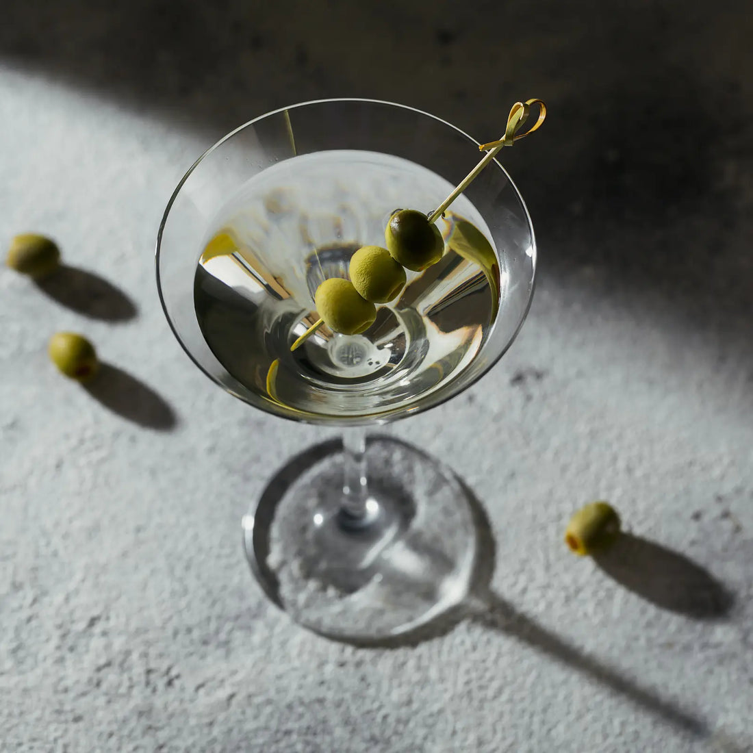 Classic extra dry vodka martini garnished with three green olives, served on a textured surface in moody lighting