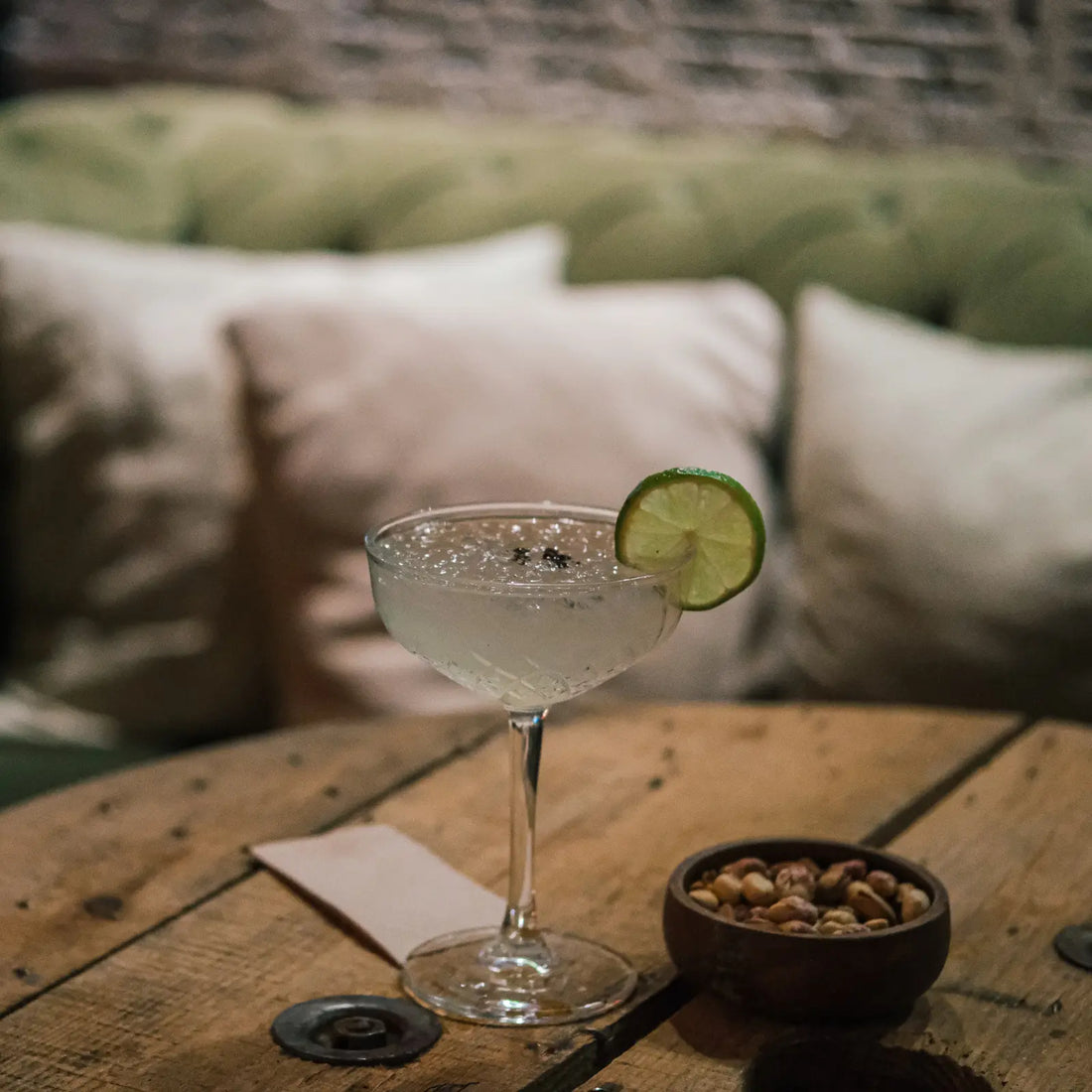 Gin gimlet cocktail with lime garnish in a coupe glass on a rustic table with pistachios