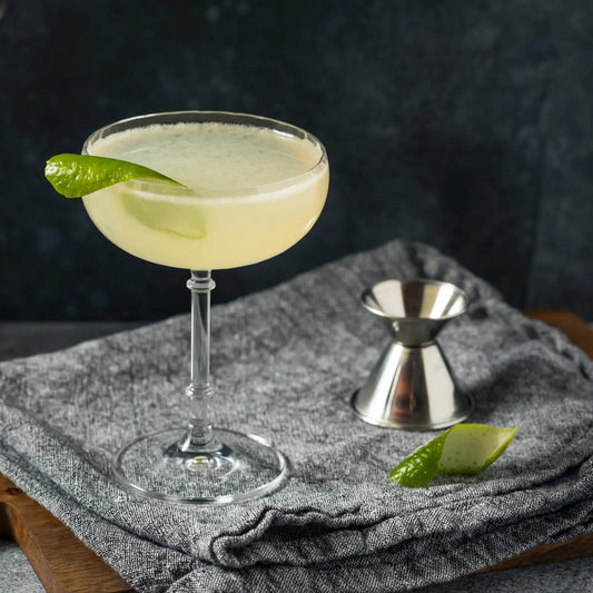 Refreshing gin cocktail with a lime peel garnish, displayed alongside a jigger on a textured cloth