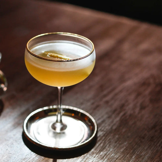 Elegant gin sour cocktail in a coupe glass with a lemon twist garnish on a wooden table