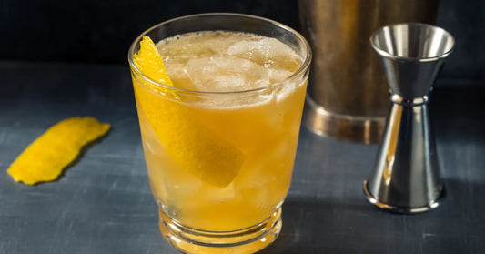 Gold Rush cocktail served over ice in a rocks glass, garnished with a lemon peel, alongside bartending tools