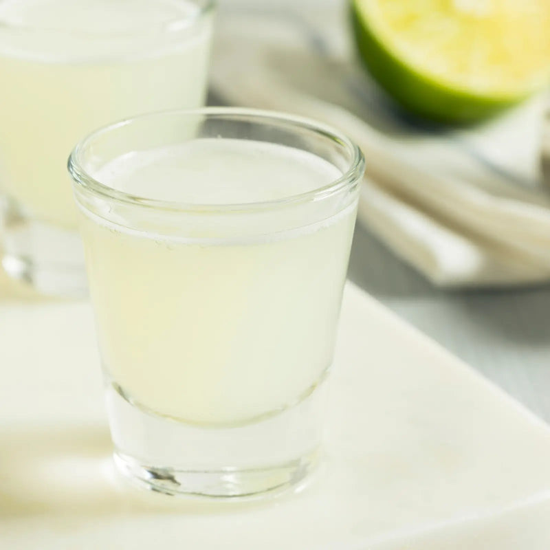 Pale citrus Kamikaze shot in a glass beside a fresh lime half.