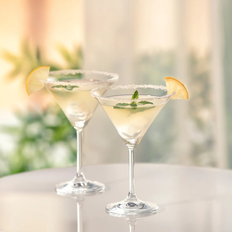 Two sugar-rimmed lemon drop martinis garnished with lemon wheels and mint on a bright table.