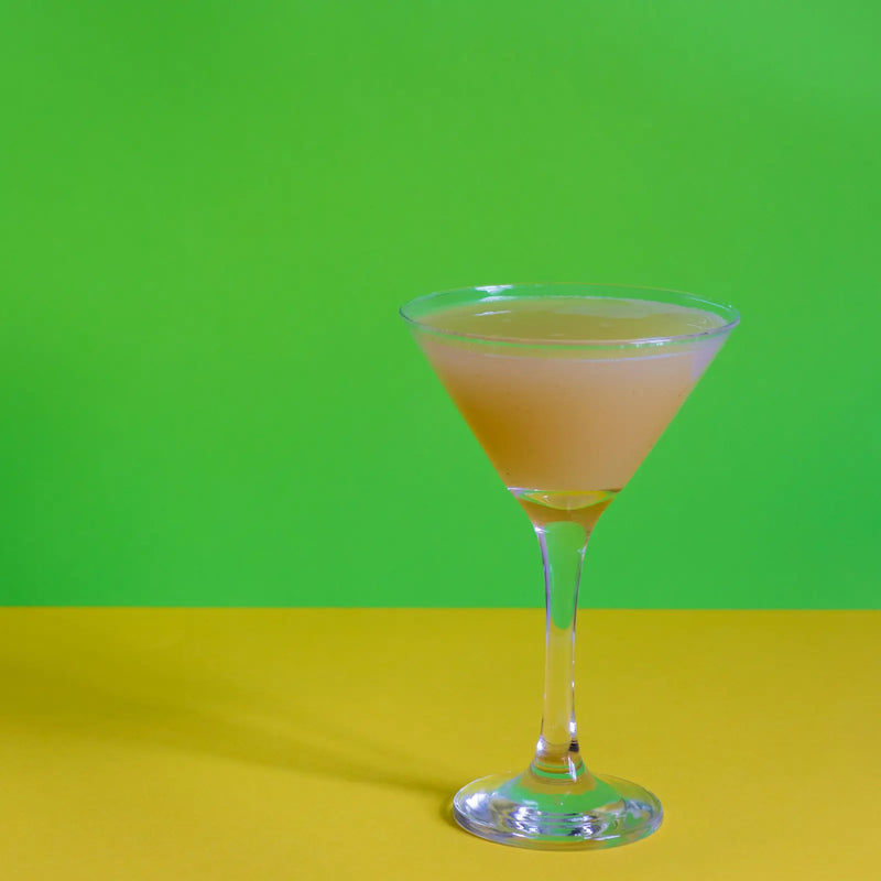 Pale pear martini in a stemmed glass against a green and yellow backdrop.