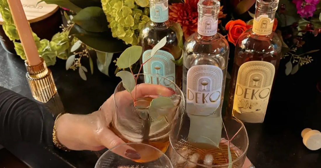 Bottled cocktails lineup of Deko surrounded by flowers and glasses in a celebratory toast.