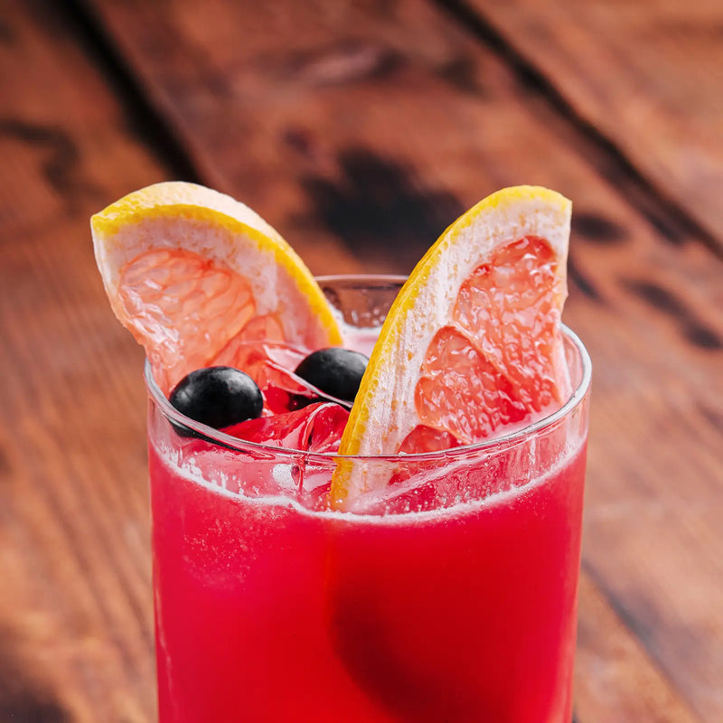 Close-up of a red Sea Breeze cocktail garnished with grapefruit slices and blueberries.