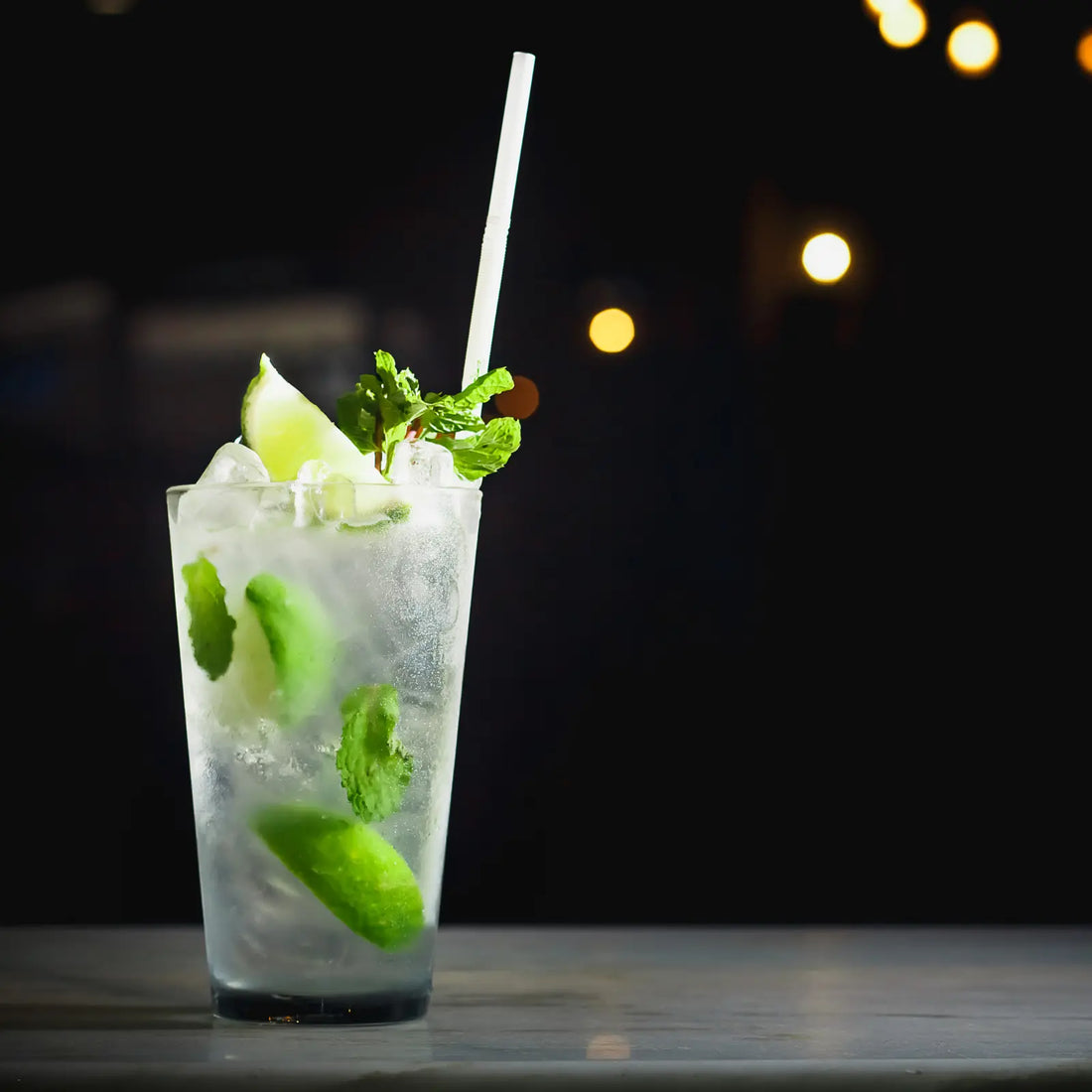 vodka mojito cocktail in a tall glass with lime and mint garnish against a dark background