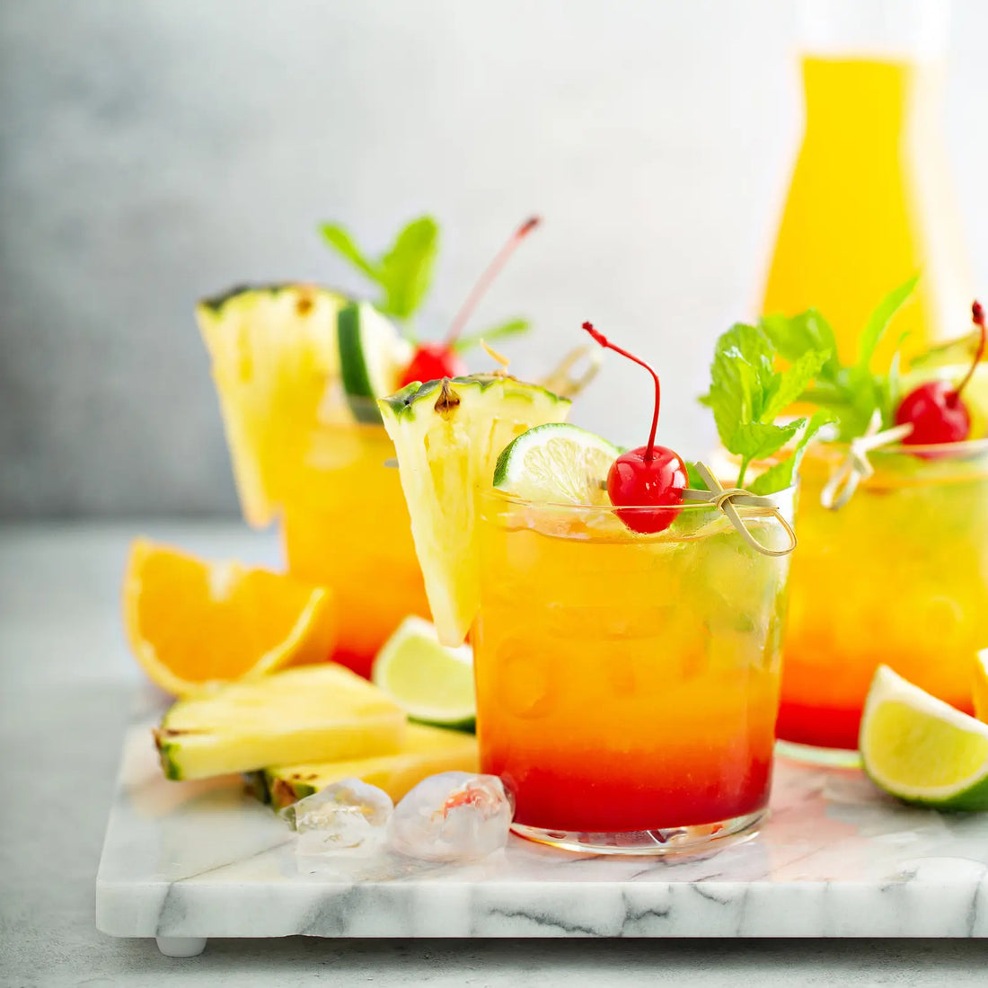 vodka sunrise cocktails with pineapple, cherry, lime, and mint garnishes, served in vibrant layers on a marble tray