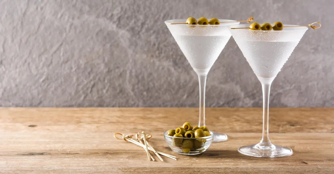 Classic martini cocktail recipe featuring two chilled martini glasses with olives, set on a rustic wooden surface.