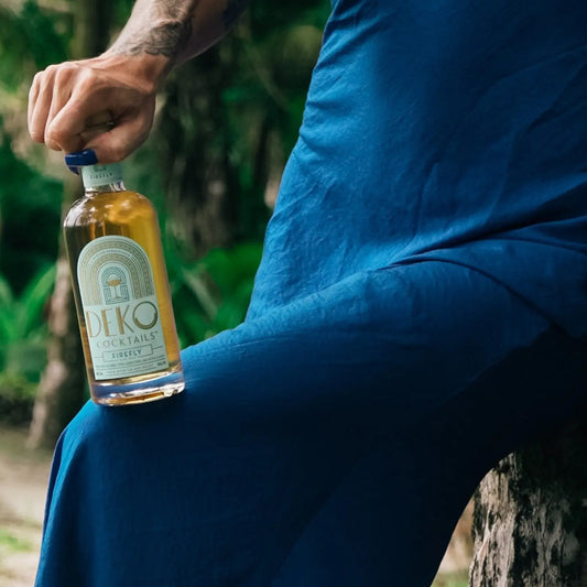 Firefly cocktail bottle held against a blue dress outdoors with a lush forest background