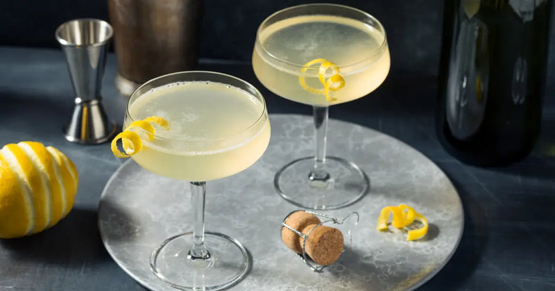 French 75 cocktail featuring gin, champagne, and lemon garnish served in coupe glasses on a silver tray