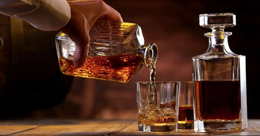 Honey bourbon drink being poured from a decanter into a glass with rustic wooden background