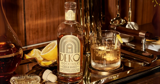 Premium craft bourbon bottle of Deko Cocktails Gold Rush with a whiskey glass and fresh lemon garnish on a bar tray.