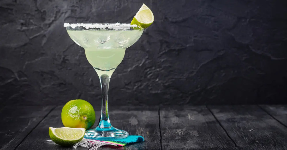 Summer cocktails served in a salt-rimmed glass with fresh lime garnish and whole limes on the table.