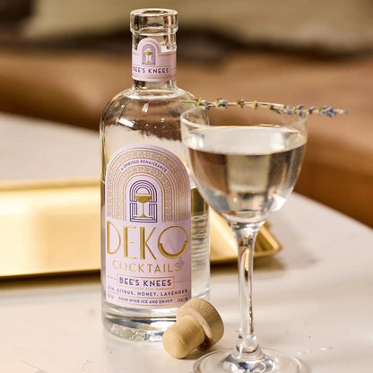 Bee's Knees gin cocktail bottle with lavender-garnished coupe glass and gold tray.