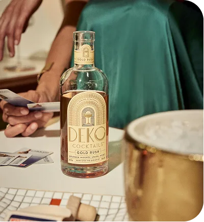 Deko Cocktails Gold Rush bourbon bottle on a bar table beside a gold ice bucket.