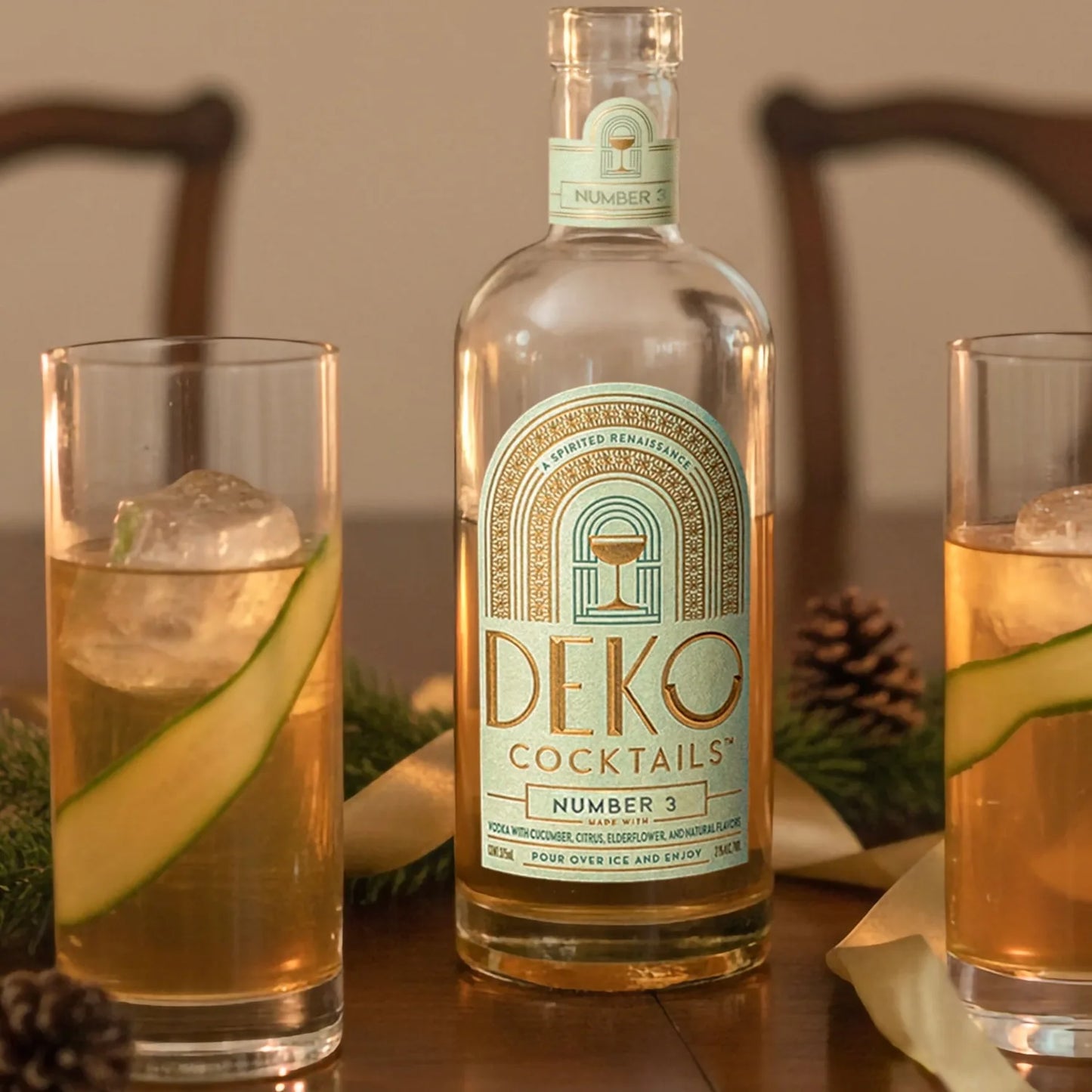 Deko Number 3 cucumber vodka cocktail bottle on a wood table with two tall glasses over ice and cucumber ribbons.