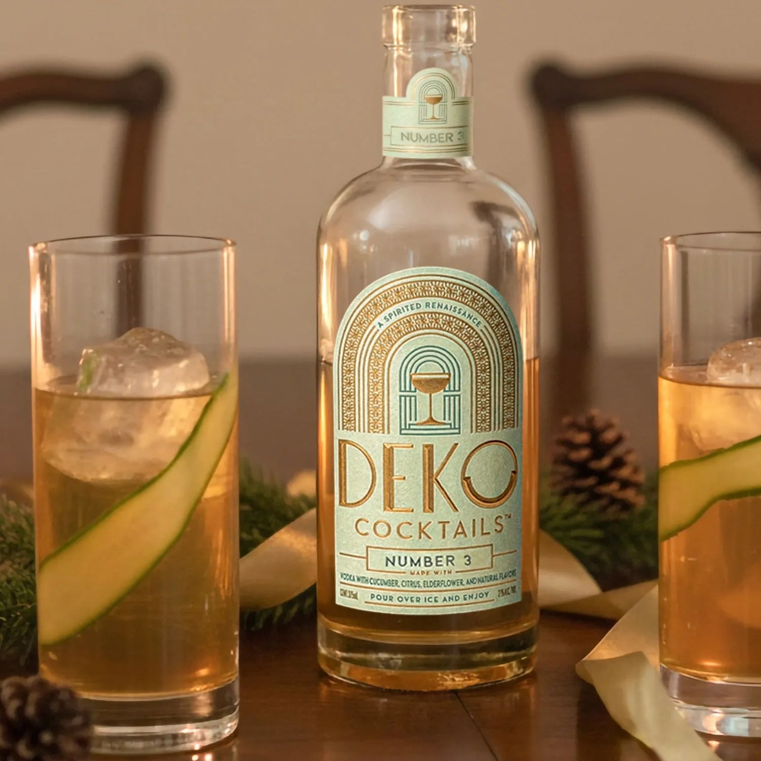 Deko Number 3 cucumber vodka cocktail bottle on a wood table with two tall glasses over ice and cucumber ribbons.